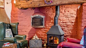 A cozy room with a stone wall, a fireplace, a log stove, leather furniture, and a wicker basket labeled 'WOOD'. - 2 Bed in Craven Arms (oc-83166) (Clun)