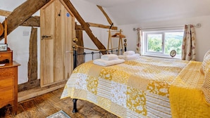 A bedroom with a sloped ceiling, a bed with a patterned bedspread, a wooden wardrobe, a hanging light fixture, and a window with a view. - 2 Bed in Craven Arms (oc-83166) (Clun)