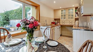 A kitchen with a dining area, a window with a view of greenery, and a vase with flowers on the table. - 2 Bed in Craven Arms (oc-83166) (Clun)