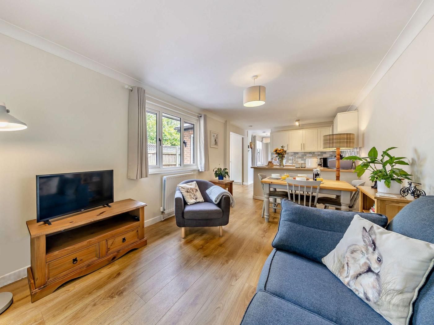 Un salon moderne doté d’un téléviseur à écran plat, d’un canapé, d’un meuble de rangement en bois et d’un coin repas avec une table et des chaises.