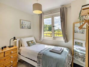 A bedroom with a bed, a bedside lamp, a dresser, a window with curtains, and a mirror with a plant. - 2 Bed in Crewe (oc-83192) (Audlem)