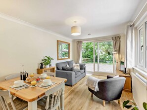 A cozy living room with a sofa, a dining table set for breakfast, and a large window with curtains. - 2 Bed in Crewe (oc-83192) (Audlem)