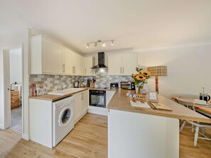 A modern kitchen with white cabinetry, a built-in washing machine, and a central island with a coffee maker. - 2 Bed in Crewe (oc-83192) (Audlem)