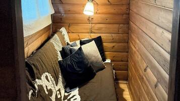 Um quarto pequeno e acolhedor, com decoração em madeira, uma cama com colcha estampada, uma luminária na parede e uma janela com cortina.
