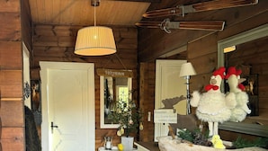 Interno di una baita in legno con una porta bianca, uno specchio, un comò e una lampada a sospensione.