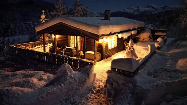 Una baita di legno con un portico, paesaggi innevati e montagne sullo sfondo.