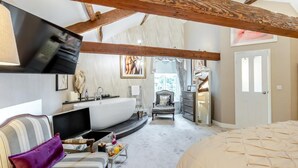Ein Schlafzimmer mit einem großen Bett, einem gewölbten weißen Waschbecken, einem Sessel und einem Fernseher.