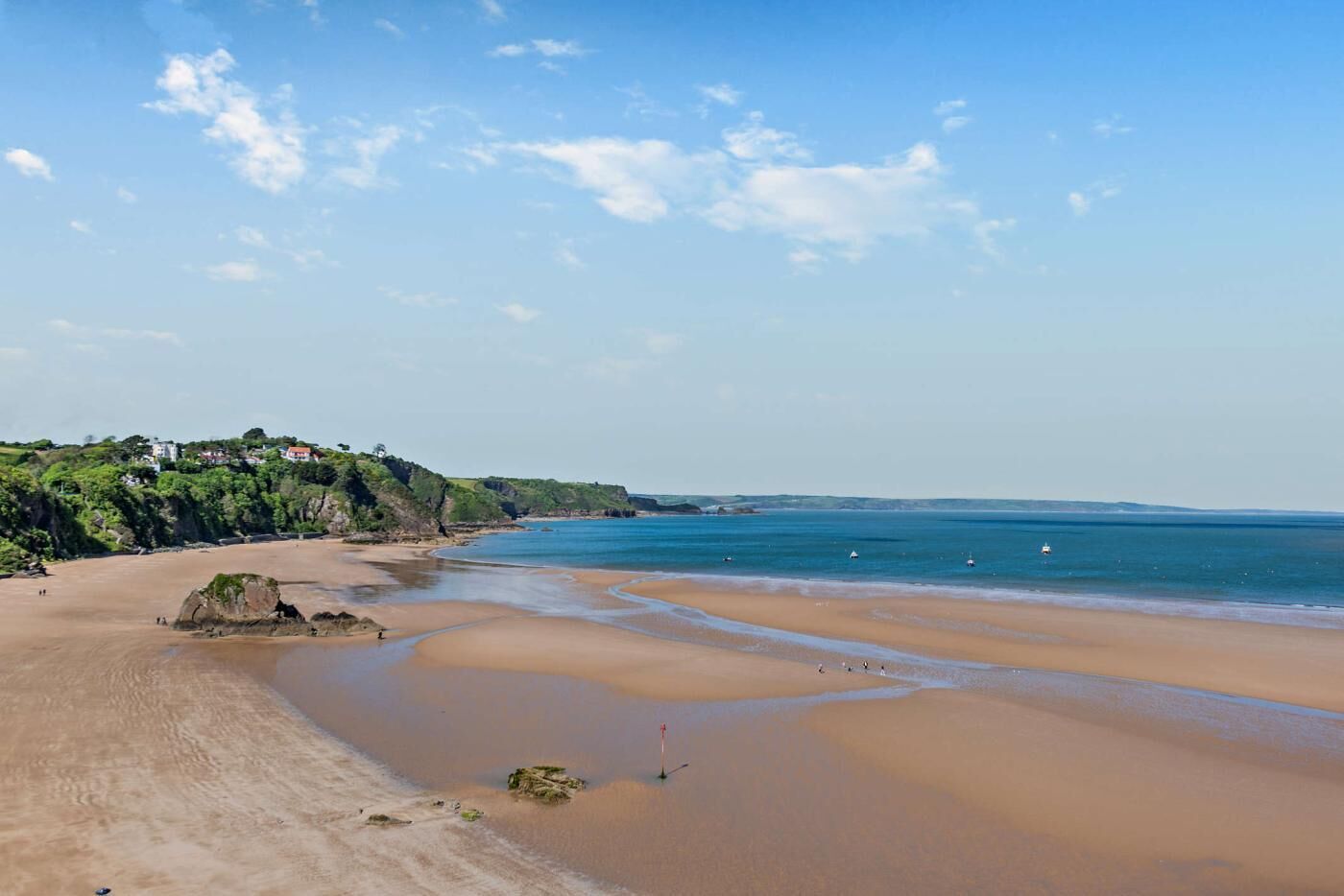 A coastal beach with a sandy shore, a clear sky, and a distant view of houses on a cliff.
