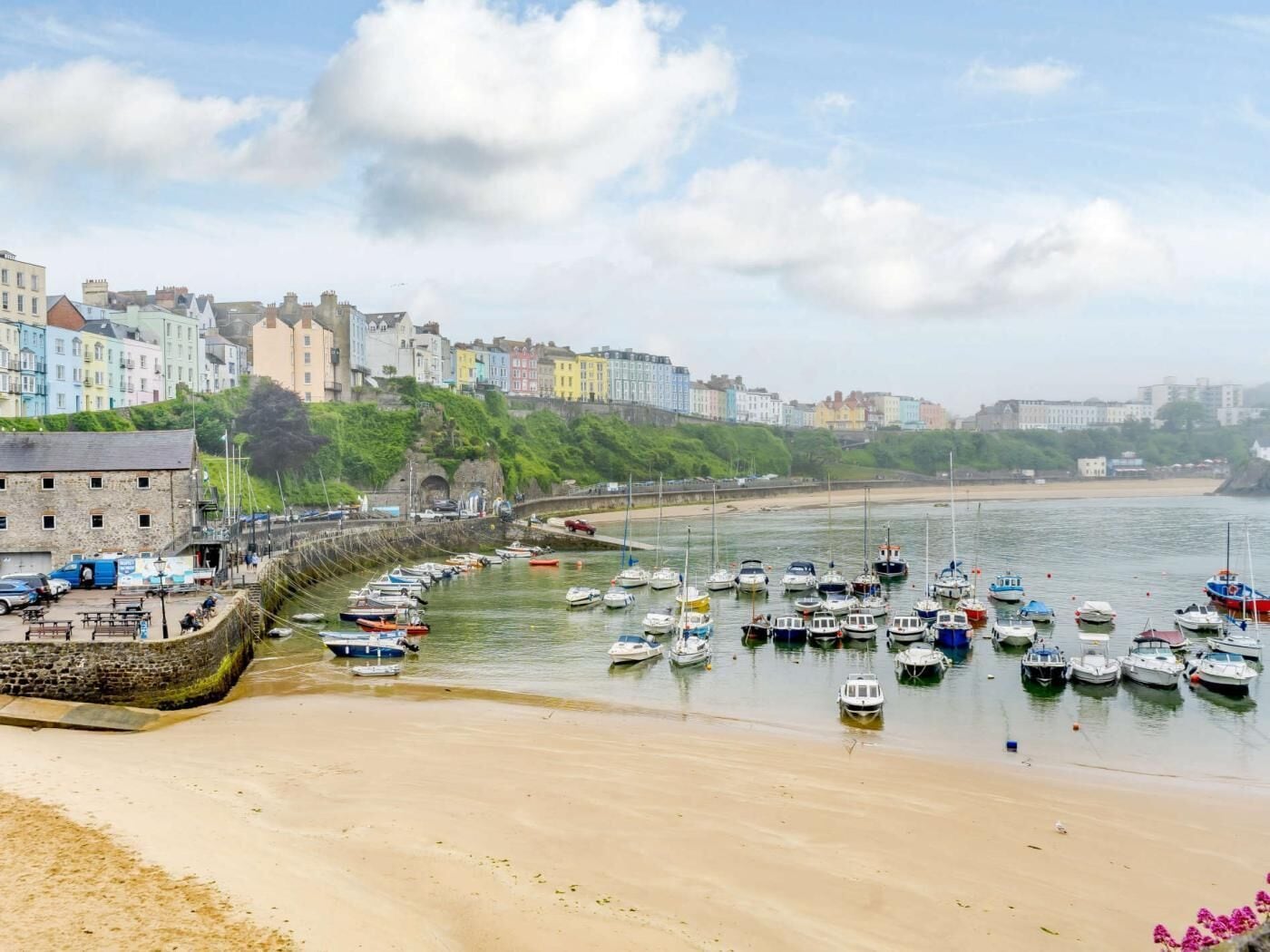 A coastal town with colorful buildings, a sandy beach, and numerous boats docked along the shore.