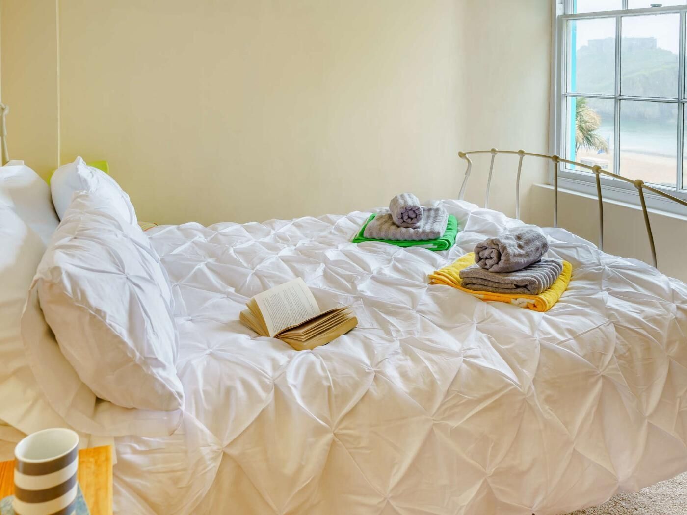A neatly made bed with a book, towels, and a cup.