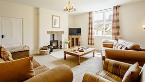 A cozy living room with a fireplace, sofa, television, and a window with curtains. - 3 Bed in Great Ayton (oc-83328) (Great Ayton)