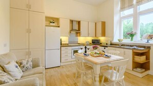 Una cocina moderna con armarios blancos, una mesa de comedor con sillas y una ventana con cortinas.