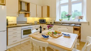 Una cocina moderna con armarios blancos, horno empotrado, microondas y un comedor con una mesa dispuesta para dos.