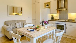 Una cocina compacta con muebles blancos, extractor de acero inoxidable y una mesa de comedor de madera con sillas.