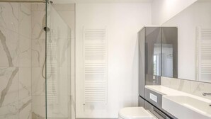 Ein modernes Badezimmer mit Duschkabine aus Glas, einer weißen Toilette und einem großen Spiegel über einem weißen Waschbecken.