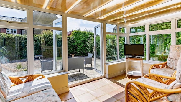 A sunlit room with large windows, a television, wicker furniture, and a tiled floor. - 2 Bed in Moreton In Marsh (oc-83379) (Blockley)