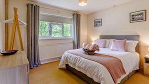 A bedroom with a bed, a bedside table, a window with curtains, a radiator, and a painting on the wall. - 2 Bed in Moreton In Marsh (oc-83379) (Blockley)