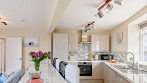 A modern kitchen with a central island, built-in appliances, and a dining area with a sofa. - 2 Bed in Woolacombe (oc-83425) (Woolacombe)