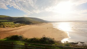 A coastal landscape with a sandy beach, rolling hills, and a clear sky. - 2 Bed in Woolacombe (oc-83425) (Woolacombe)