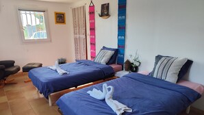 Hotellihuone, jossa on kaksi sänkyä, tuoli, pieni pöytä ja ikkuna, jossa on sälekaihtimet.
