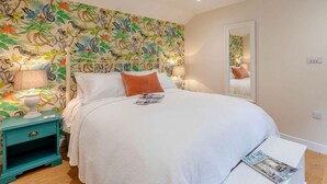 A bedroom with a bed, a nightstand, a mirror, and a wall with a floral pattern. - 1 Bed in Wincanton (oc-83499) (Holton)