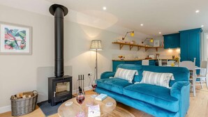 A living room with a sofa, a round coffee table, a fireplace, and a kitchen area in the background. - 1 Bed in Wincanton (oc-83499) (Holton)