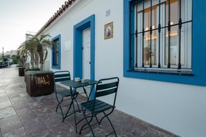 Ein Außenbereich mit Tisch und Stühlen, einem Blumentopf und einem Gebäude mit blauen Türen und Fenstern.