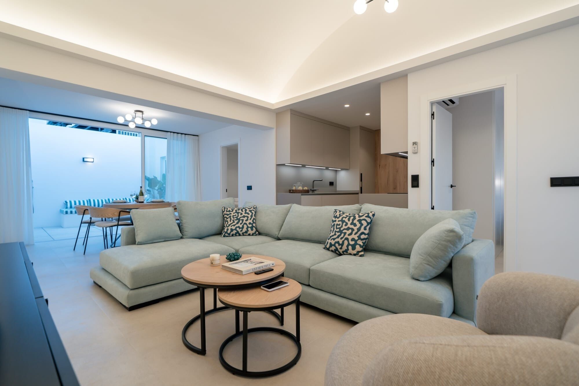 A modern living room with a sectional sofa, a round coffee table, and a dining area with a table and chairs.