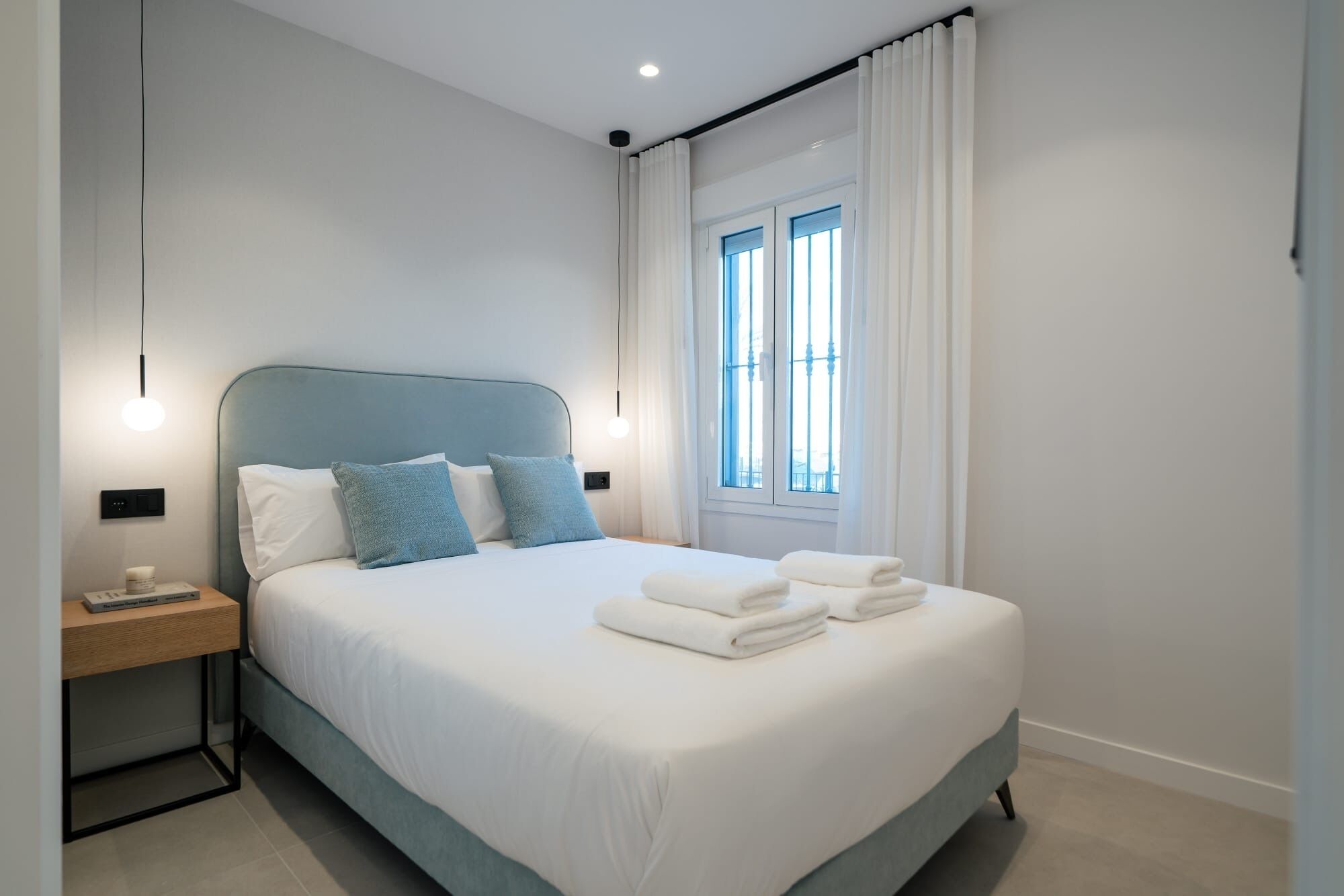 A modern bedroom with a bed, pillows, a nightstand, and a window with curtains.