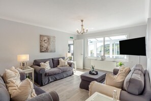 Ein modernes Wohnzimmer mit einem grauen Sofagarnitur, einem Couchtisch, einem an der Wand montierten Fernseher und einer Kronleuchter.