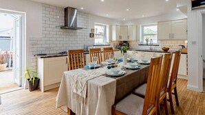 Une cuisine moderne avec des meubles blancs, un îlot central et un coin repas avec une table dressée pour six personnes.