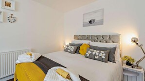 Un lit bien fait, avec une tête de lit, une lampe de chevet et une horloge murale.