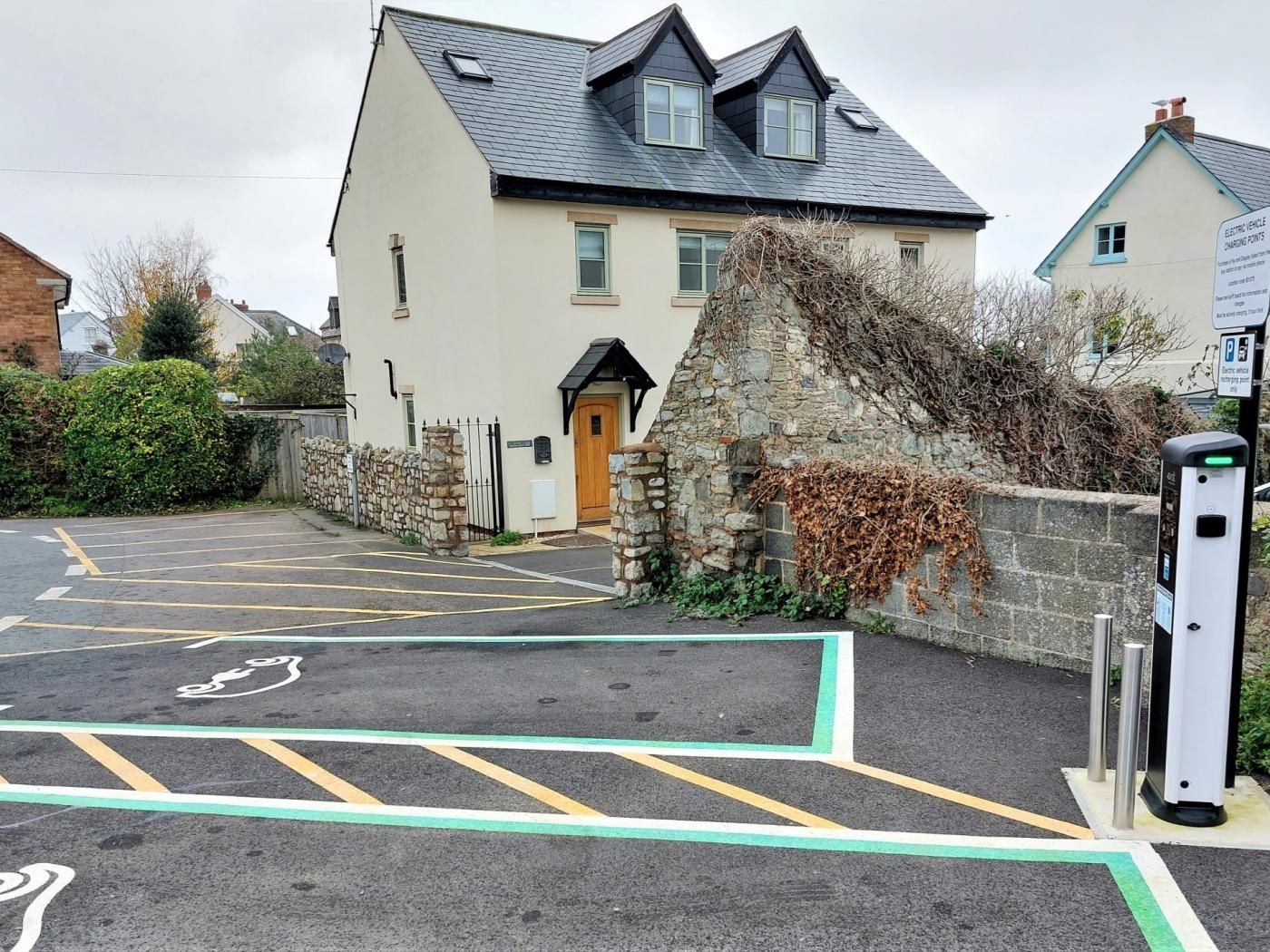 A parking area with marked spaces, a stone wall, and a building with a pitched roof.