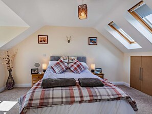 A bedroom with a sloped ceiling, a bed with plaid bedding, two bedside lamps, a wall-mounted deer head, and a skylight. - 3 Bed in Watchet (oc-83532) (Watchet)
