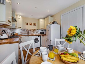 A modern kitchen with a dining area, including a stove, sink, washing machine, and refrigerator. - 3 Bed in Watchet (oc-83532) (Watchet)