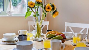 A breakfast table with a vase of sunflowers, fruit bowl, and various breakfast items. - 3 Bed in Watchet (oc-83532) (Watchet)