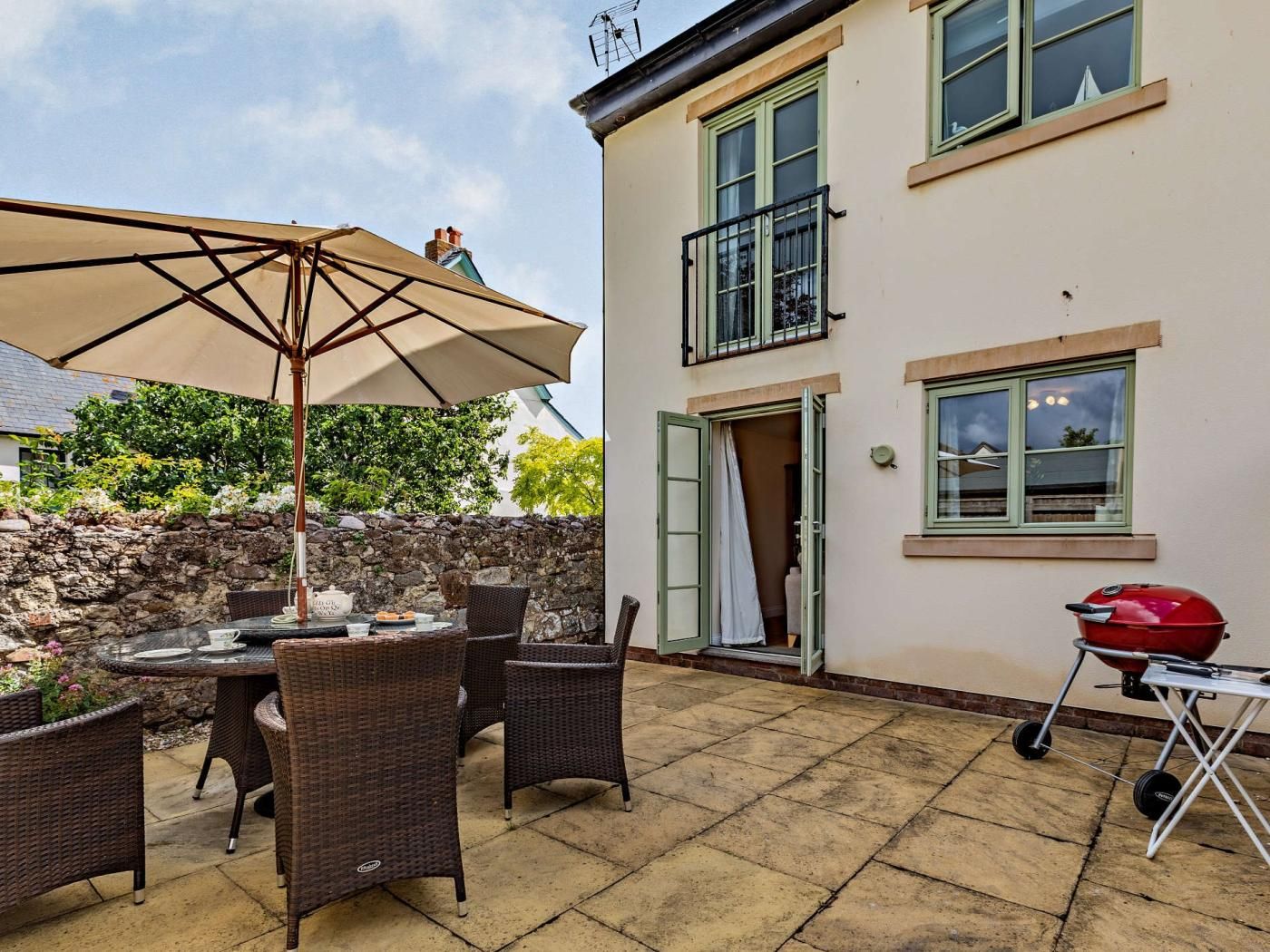 Eine Terrasse mit Korbmöbeln, einem Tisch und einem Grill.
