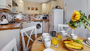 A modern kitchen with a dining area, including a stove, sink, washing machine, and refrigerator. - 3 Bed in Watchet (oc-83532) (Watchet)