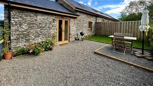 A stone building with a gravel patio, a wooden door, and a barbecue grill. - 1 Bed in Aberystwyth (oc-83551) (Llanilar)