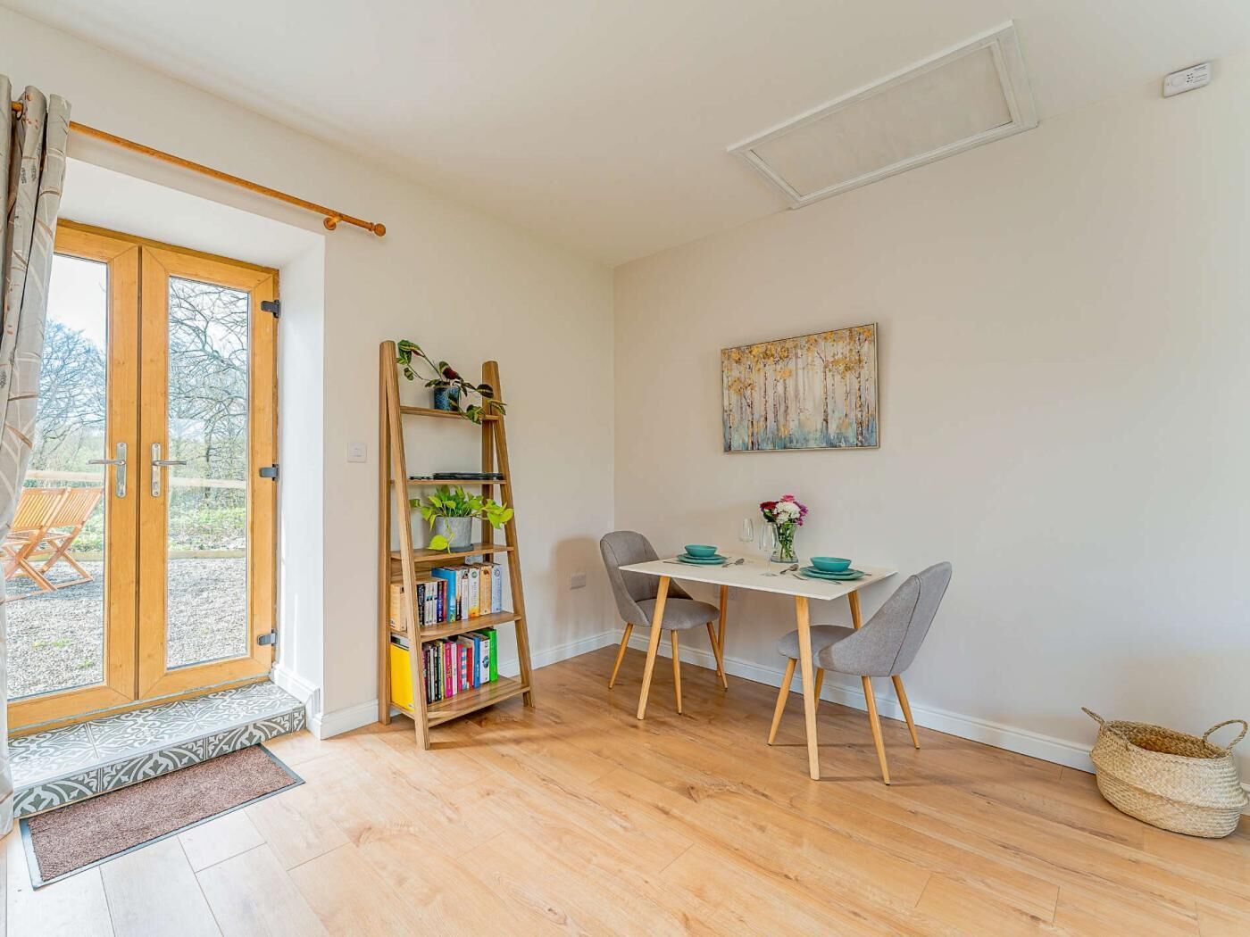 Una habitació amb sòl de fusta, una taula de dinar amb caires, una biblioteca i un quadre a la paret.