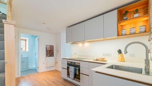 A modern kitchen with grey cabinets, a white countertop, a built-in oven, and a wooden shelf with plants. - 1 Bed in Aberystwyth (oc-83551) (Llanilar)