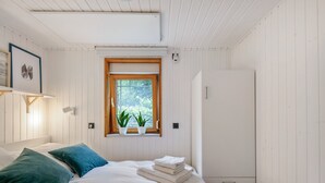 Una camera da letto con un letto, due cuscini, una finestra con piante, un armadio e un condizionatore d'aria a parete.