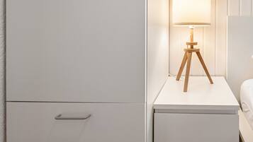 A white bedside table with a lamp, a drawer, and a bed.