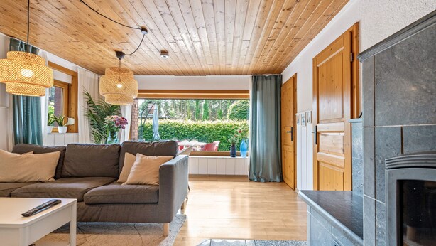 Un soggiorno con soffitto in legno, un camino, un divano e vista sul verde.