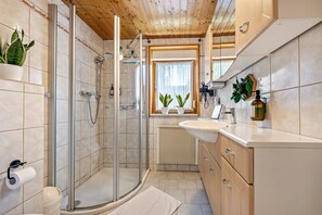 A modern bathroom with a glass-enclosed shower, a white sink, wooden cabinets, and potted plants. - Holiday Home 'Wald-See-Liebe' with Private Terrace and Private Garden (Schenkendöbern)