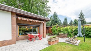 Un patio con un muro in mattoni, una porta vetrata e un tavolo con sedie rosse.