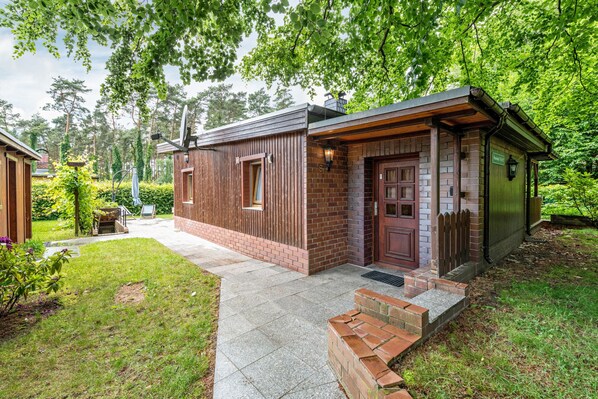 A two-story wooden cabin with a brick entrance, surrounded by a well-maintained garden and trees. - Holiday Home 'Wald-See-Liebe' with Private Terrace and Private Garden (Schenkendöbern)