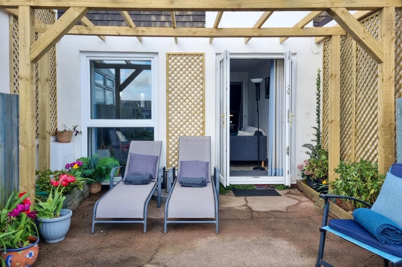 A covered patio with two lounge chairs, a small table, and potted plants.