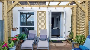 En overdækket terrasse med to liggestole, et lille bord og plantekrukker.
