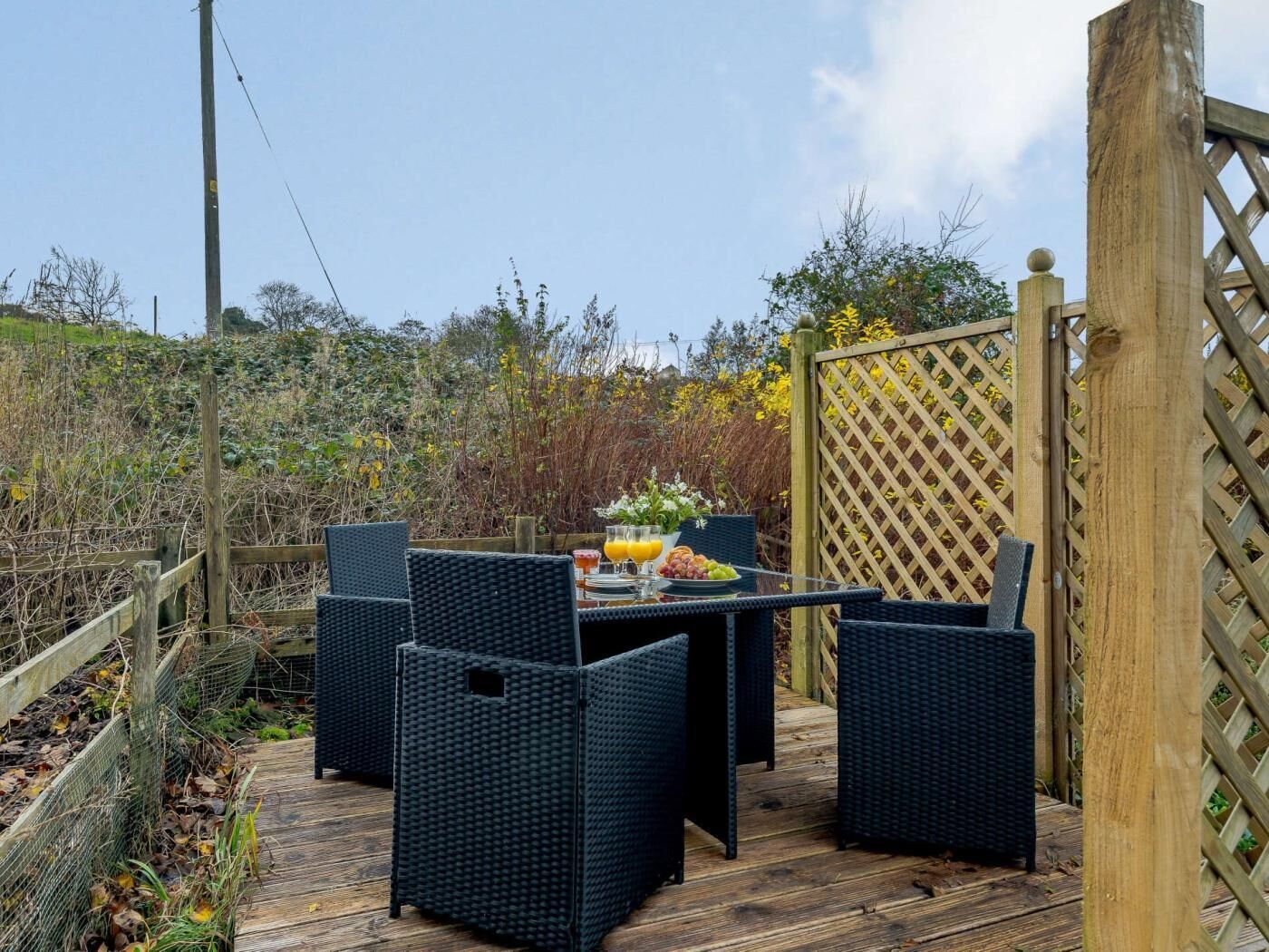 Een terras buiten met rieten meubels, een tafel met een fruitschaal, en een houten omheining.